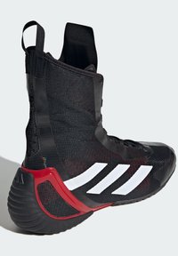 Black athletic shoe featuring a high-top design, textured fabric, and prominent white stripes. Red accents on the heel and sole enhance detail.
