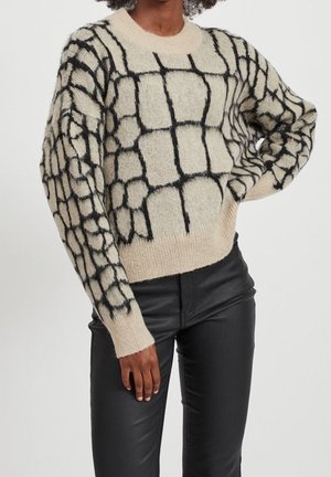 Pull beige avec un motif en grille noir, fabriqué à partir d'un matériau texturé ; il possède un col rond et des manches amples.