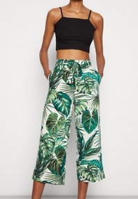Pantalon large à motif tropical avec taille nouée, présentant des feuilles vertes sur un fond clair. Tissu doux avec poches.