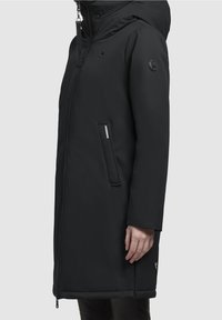 Parka negra aislante con capucha, bolsillos laterales y un discreto logo. Textura suave, mangas largas y cierre frontal con cremallera.