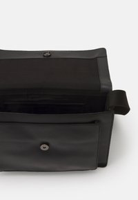 Borsa a tracolla rettangolare nera con pattina aperta, che mostra una tasca interna e chiusura a bottone magnetico.