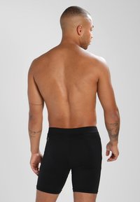 Sorte svømmeshorts laget av glatt, elastisk materiale. Har et enkelt design med en tettsittende passform og elastisk midje.