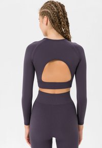 Purple long-sleeve sports top with a cut-out back and ribbed texture, paired with matching high-waisted leggings.