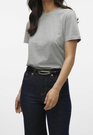 Kvinde iført en ensfarvet grå T-shirt med korte ærmer, stoppet ned i mørkeblå jeans med et sort bælte med en guldfarvet oval spænde.