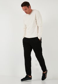 Cremfarbens Langarmshirt, schwarze elastische Bundhose und schwarze Sneakers mit weißen Sohlen. Glatte Texturen, lockere Passform, minimalistisches Design.