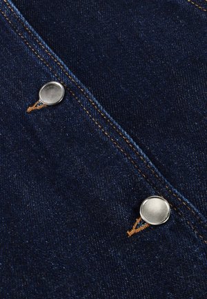 Dunkelblaue Denim-Stoff mit silbernen Druckknöpfen, orangefarbenen Nähten und einer strukturierten Oberfläche. Der Stoff zeigt leichte Farbvariationen.