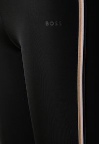 Leggings sportivi neri con un piccolo logo "BOSS", strisce orizzontali in oro e bianco, e una texture liscia e elastica.