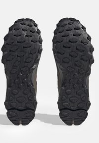 Semelle en caoutchouc noire avec des crampons de traction multidirectionnels. Le design présente diverses textures et motifs pour une meilleure adhérence sur des surfaces variées.