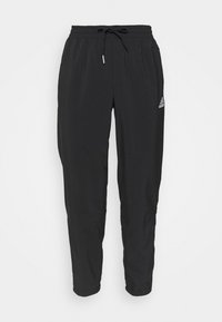 Černé sportovní kalhoty s elastickým pasem, stahovací šňůrkou a elastickými manžetami. Na boku se nachází malé bílé logo Adidas.