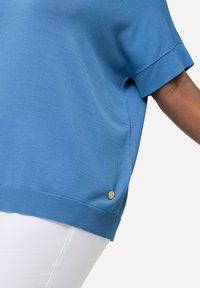 Kortärmad blå tröja i ett mjukt tyg med ribbad fåll, med en liten guldfärgad detalj på sidan.