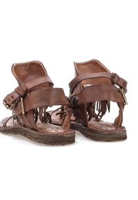 Brune lædersandaler med en åben hæl, flere stropper, dekorerende nitter og en tekstureret sål. Der er detaljeret syning på siden.
