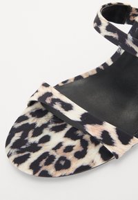Sandale plate à imprimé léopard avec une semelle noire, des sangles croisées et une texture de tissu lisse. Le design met en avant un motif audacieux inspiré des animaux.