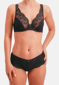 Schwarzes Spitzen-Dessous-Set mit V-Ausschnitt-BH mit Blumenmuster und passendem Slip mit gewellten Kanten. Silberne Akzentdetails in der Mitte.