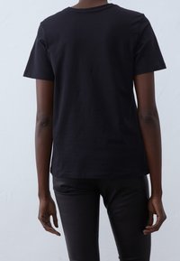 T-shirt en coton noir à manches courtes, col rond et coupe décontractée. Couleur unie, texture lisse, sans motifs ni embellissements visibles.