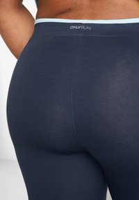 Granatowe legginsy wykonane z elastycznego materiału, z jasnoniebieskim pasem w talii z logo "ONLY PLAY". Gładka tekstura z minimalnymi szwami.