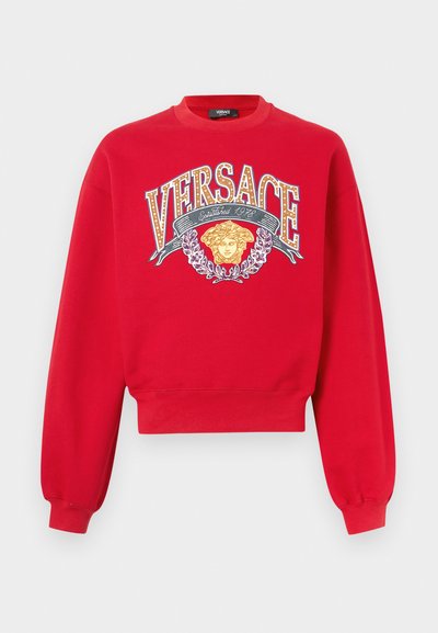 Punane lühike särk, kus on suur trükitud Versace logo, kuldsed detailid ja graafiline disain peadeemoti ning lauruoksidega.