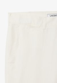 Pantaloni in twill di cotone bianco con frontale piatto, tasche laterali e etichetta in vita. Texture liscia e design sartoriale.