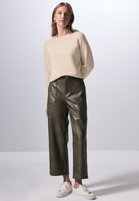 Pull en tricot beige à col rond, associé à un pantalon large en simili cuir vert foncé taille haute et des baskets blanches.