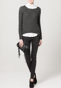 Grijze gebreide trui met een textuurdesign, gedragen over een witte blouse met kraag. Gemaakt met zwarte skinny jeans en een gefranjeerde zwarte clutch.