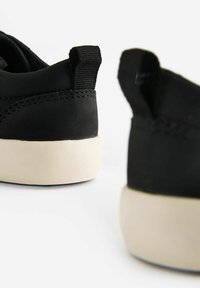 Zwarte sneakers met een glad bovendeel, contrasterende witte rubberen zool en een achterste trekband voor gemakkelijk aantrekken; minimalistisch ontwerp met subtiele stiksels.