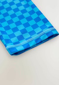 Blauw geruit zwemkledingstof met een gladde textuur, met licht- en donkerblauwe vierkanten. De zoom is gestikt met contrasterende blauwe draad.