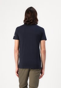 T-shirt blu navy a maniche corte con collo a giro, realizzato in un tessuto morbido, con un logo sottile sulla manica sinistra. Texture liscia.