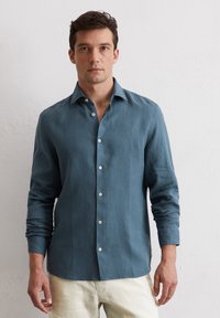 Blaues Leinenhemd mit langen Ärmeln, Knopfleiste vorn und klassischem Kragen. Verfügt über weiße Knöpfe und ein seitliches Etikett für Details.