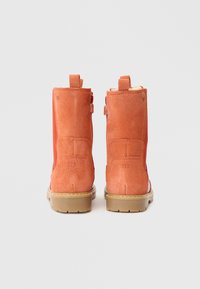 Botins de camurça laranja até ao tornozelo com um acabamento texturizado, uma sola de borracha castanha e duas alças na parte traseira para facilitar o calçar.