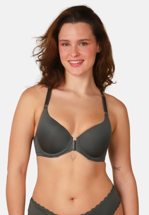 Lächelnde Frau mit welligem braunem Haar, die einen dunkelgrauen BH mit Frontverschlus und passende Unterwäsche vor einem schlichten weißen Hintergrund trägt.