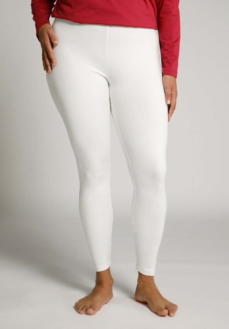 Leggings bianchi realizzati in un tessuto elasticizzato, con una superficie liscia e design a lunghezza intera. Indossati a piedi nudi con una maglietta rossa.
