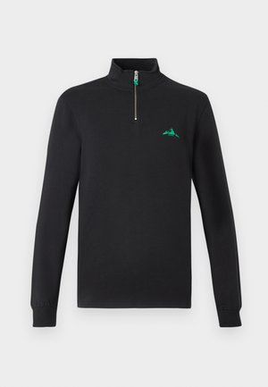 Melnā zip-augšējā flīsa džemperī ar augstu apkakli, kuram ir neliels zaļš kalna logo uz kreisās krūts un ribotām piedurknēm.