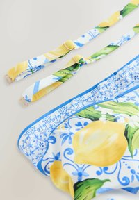 Haut de bikini avec des motifs de citrons jaunes et de feuilles vertes sur fond blanc, avec des bordures bleues et des bretelles ajustables. Détails en métal doré.