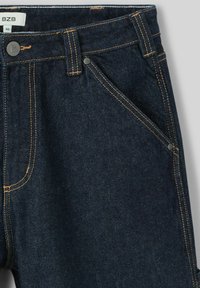Jean en denim bleu foncé avec des coutures orange contrastantes, une seule poche avant, et une fermeture à bouton avec un détail de logo.