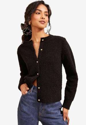 Black textured cardigan with a round neckline, featuring gold buttons along the front and long sleeves, worn over blue jeans.