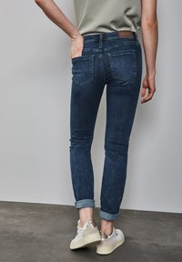 Jean skinny bleu en denim avec une texture lisse, doté de deux poches arrière et d'un ourlet retroussé, associé à des baskets légères.