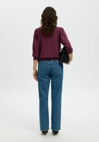 Vínová halenka s napuffovanými rukávy je kombinována s modrými džíny vysokého pasu a rovnými nohavicemi. Outfit doplňuje černá kabelka a špičaté lodičky.