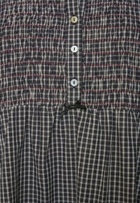 Sötétkék és krémszínű kockás mintájú ráncolt ruha, piros varrással, az elején egy sor kerek, fehér gombbal és fekete masni díszítéssel.