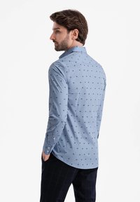 Camisa de botones azul claro con pequeños patrones en navy, mangas largas y cuello esparcido. Tejido suave con un ajuste relajado.