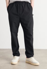 Sorte elastiske bukser med lommer på siden; glat stof og smalle ben. Parret med lyse sneakers med en tekstureret sål.