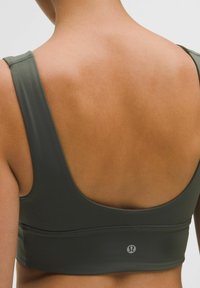 Olíva zöld sportmelltartó széles pántokkal és mély hátkivágással. Simmi, rugalmas anyag, diszkrét logóval a deréknál.