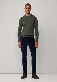 Grüner Strickpullover mit Rundhalsausschnitt, kombiniert mit navyblauen Cordhosen. Braune Lederschuhe vervollständigen das Outfit. Minimalistisches Design, strukturierter Stoff.