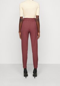 Bordové kalhoty se stahovacím pasem, tapered střih a hladkým povrchem. Nosit s černými kotníkovými botami na podpatku.