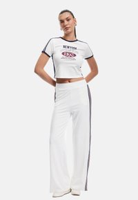 Witte cropped t-shirt met marineblauwe afwerking en grafische print, gecombineerd met witte wijde broek met zijstrepen in marineblauw. Soepele stofstructuur.