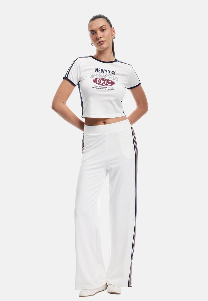 Witte cropped t-shirt met marineblauwe afwerking en grafische print, gecombineerd met witte wijde broek met zijstrepen in marineblauw. Soepele stofstructuur.