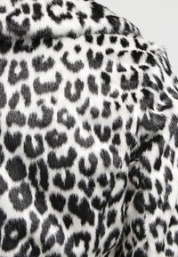 Tela de pelo sintético blanco y negro con un denso patrón de manchas de leopardo irregular, mostrada en primer plano.