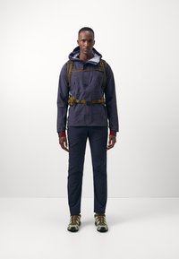 Outdoor jacket in navy, with a hood, chest pockets, and a fitted design. Paired with matching trousers and brown and green shoes.