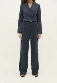 Ciemnoszara dwurzędowa marynarka z długimi rękawami, zestawiona z pasującymi szerokimi spodniami. Gładka tkanina o dopasowanym kroju; przód bez zakładek.