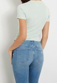 Světlonzelené přiléhavé tričko s krátkými rukávy v kombinaci s vysokými modrými džíny z denimu, které mají zadní kapsy a jemné švy.