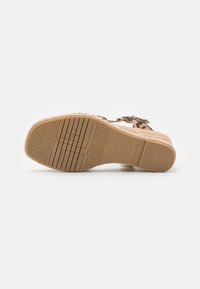 Tan sandal med et vævet jute-design og en tekstureret gummisål. Har en justerbar spænde og mønstret detaljering på sålen.
