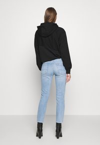 Černá mikina s kapucí v kombinaci se světle modrými skinny džíny. Džíny mají zadní kapsy a mírné vyblednutí. Černé kožené boty na podpatku dokončují outfit.